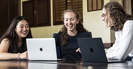 three students laughing and studying at table with laptops